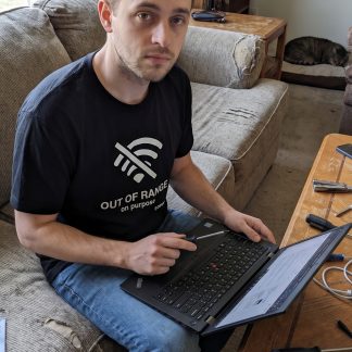 Jake Novak wearing the LOWPOWER Out of Range statement tee, fixing a neighbor laptop scene