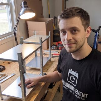 Jake Novak wearing the LOWPOWER Recurring Event statement tee, garage workbench scene