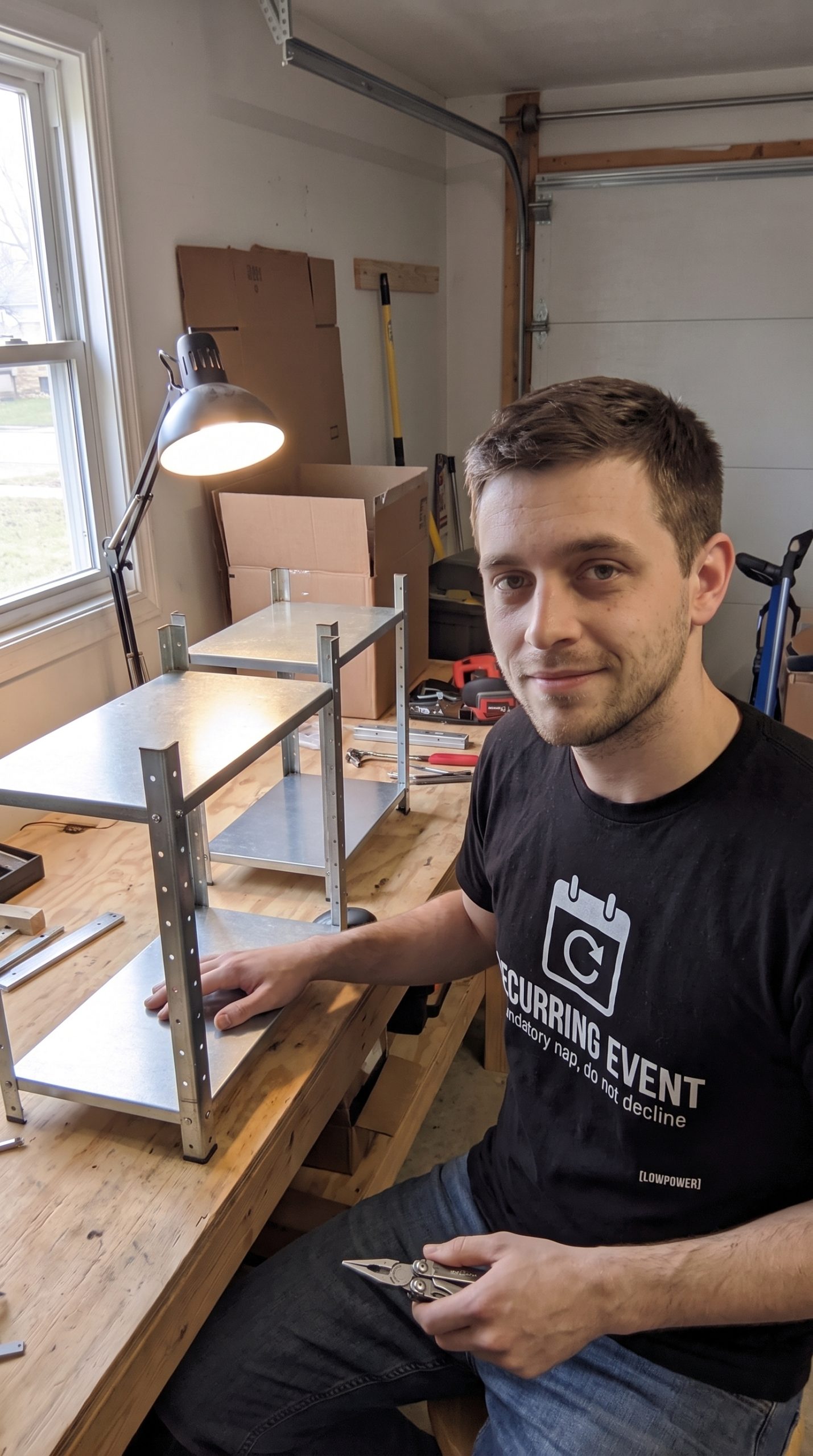Jake Novak wearing the LOWPOWER Recurring Event statement tee, garage workbench scene